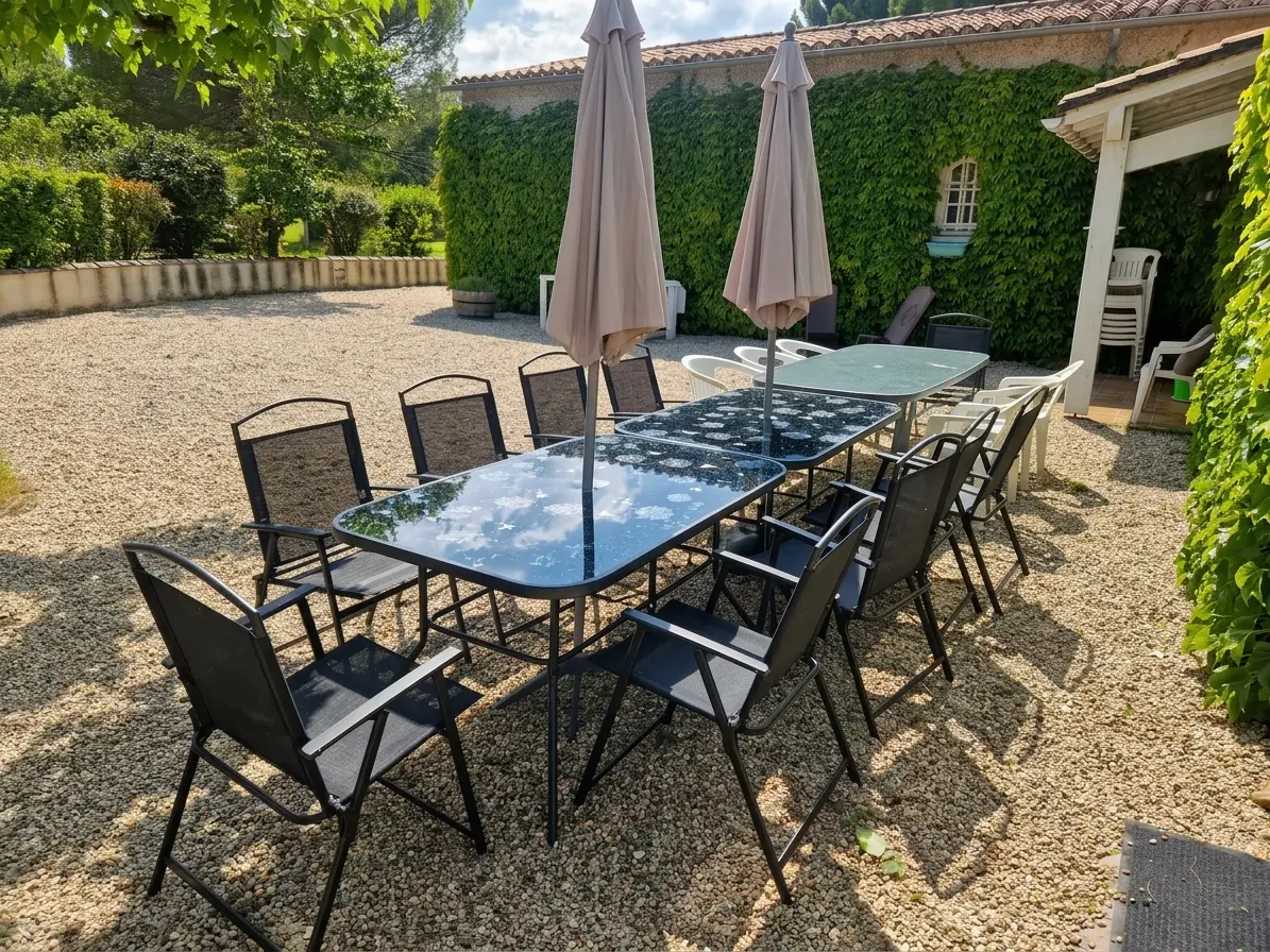 Black outdoor dining tables and chairs on the gravel terrace against the ivy-covered house wall